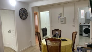 Un coin repas avec une table ronde, des chaises, une horloge et, au fond, un lave-linge.