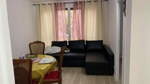Un petit salon comprenant un canapé, une table à manger avec des chaises et une fenêtre avec des rideaux.