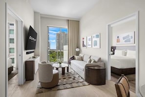 A modern hotel room with a sofa, armchair, coffee table, and a bed. There is a large window with a city view. - Prime Domus Brickell 2BR Condo (Miami)
