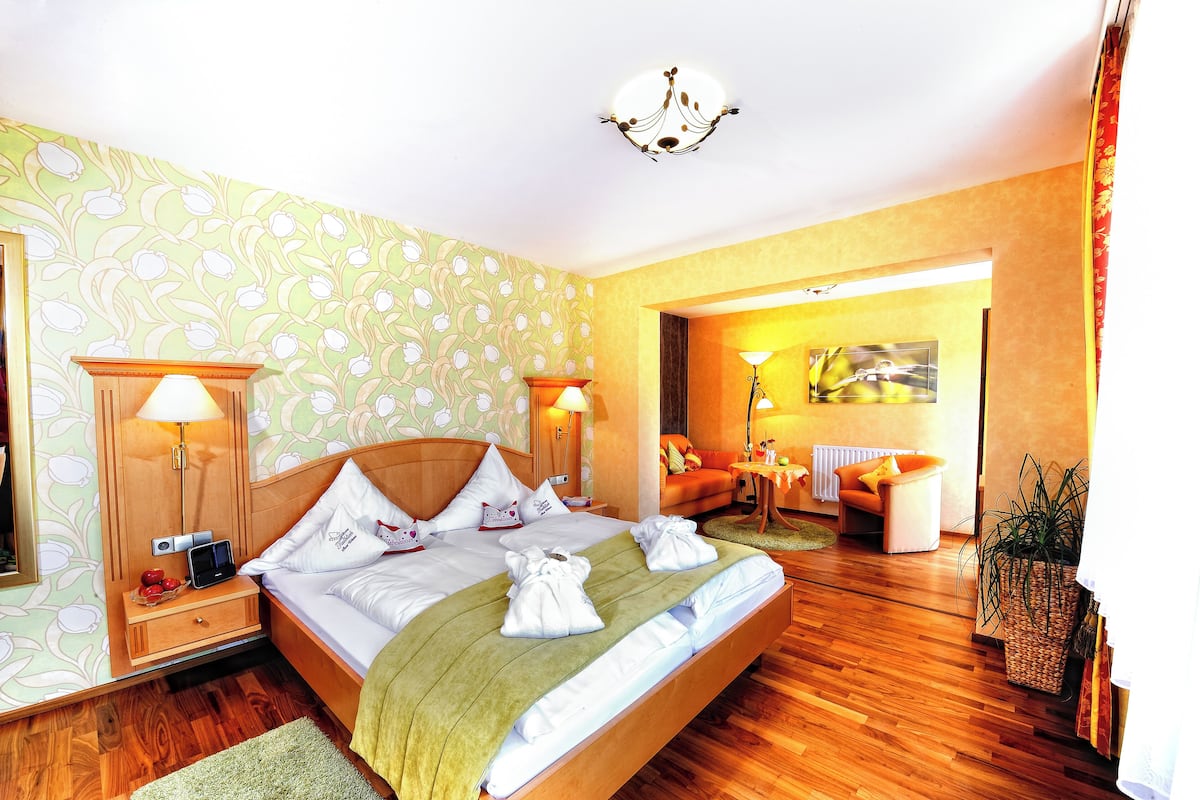 A hotel room with a bed, bedside lamps, a nightstand, a potted plant, and a view of the hallway.