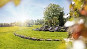A grassy outdoor area with lounge chairs arranged in a semi-circle, surrounded by a stone wall. - Landhotel Talblick  (Neuweiler)