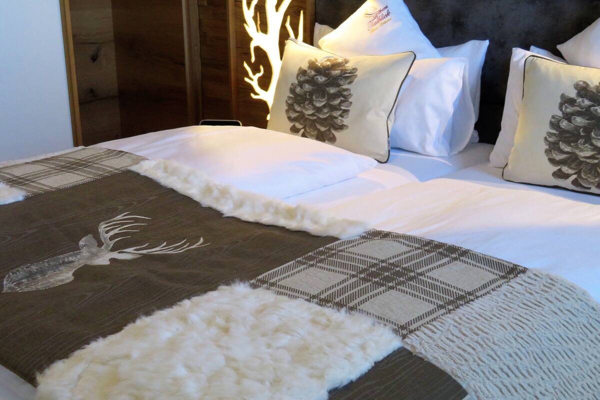 A bed with white bedding, a decorative pillow with a pinecone design, and a patterned throw.