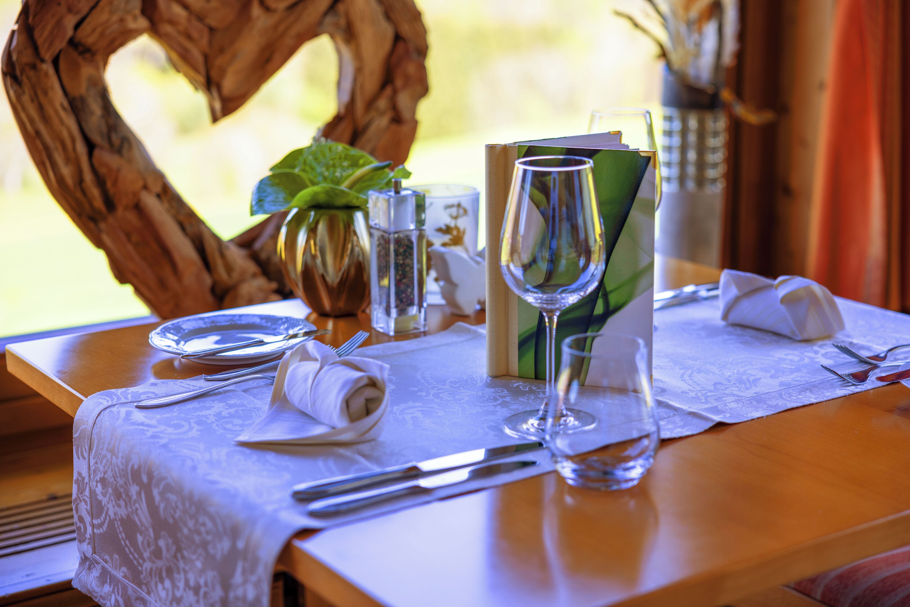 A table set with plates, cutlery, a glass, a napkin, a menu, and a decorative heart-shaped branch.