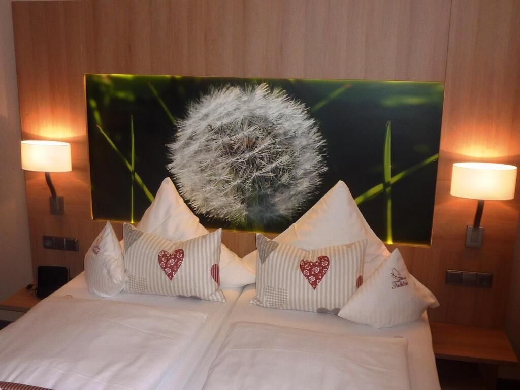 Habitación de hotel con cama, almohadas, una gran obra de arte en la pared y dos lámparas de pared.