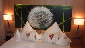 Habitación de hotel con cama, almohadas, una gran obra de arte en la pared y dos lámparas de pared.