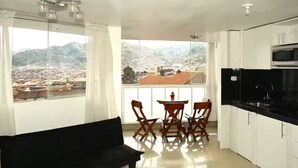 Ein Balkon mit Blick auf eine Stadtlandschaft, ein Essbereich mit Stühlen und Tisch sowie eine Küche mit Schränken und einer Mikrowelle.