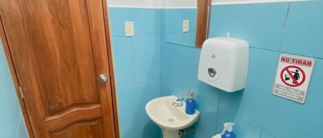 A bathroom with a wooden door, a sink, a toilet, and a hand sanitizer dispenser.