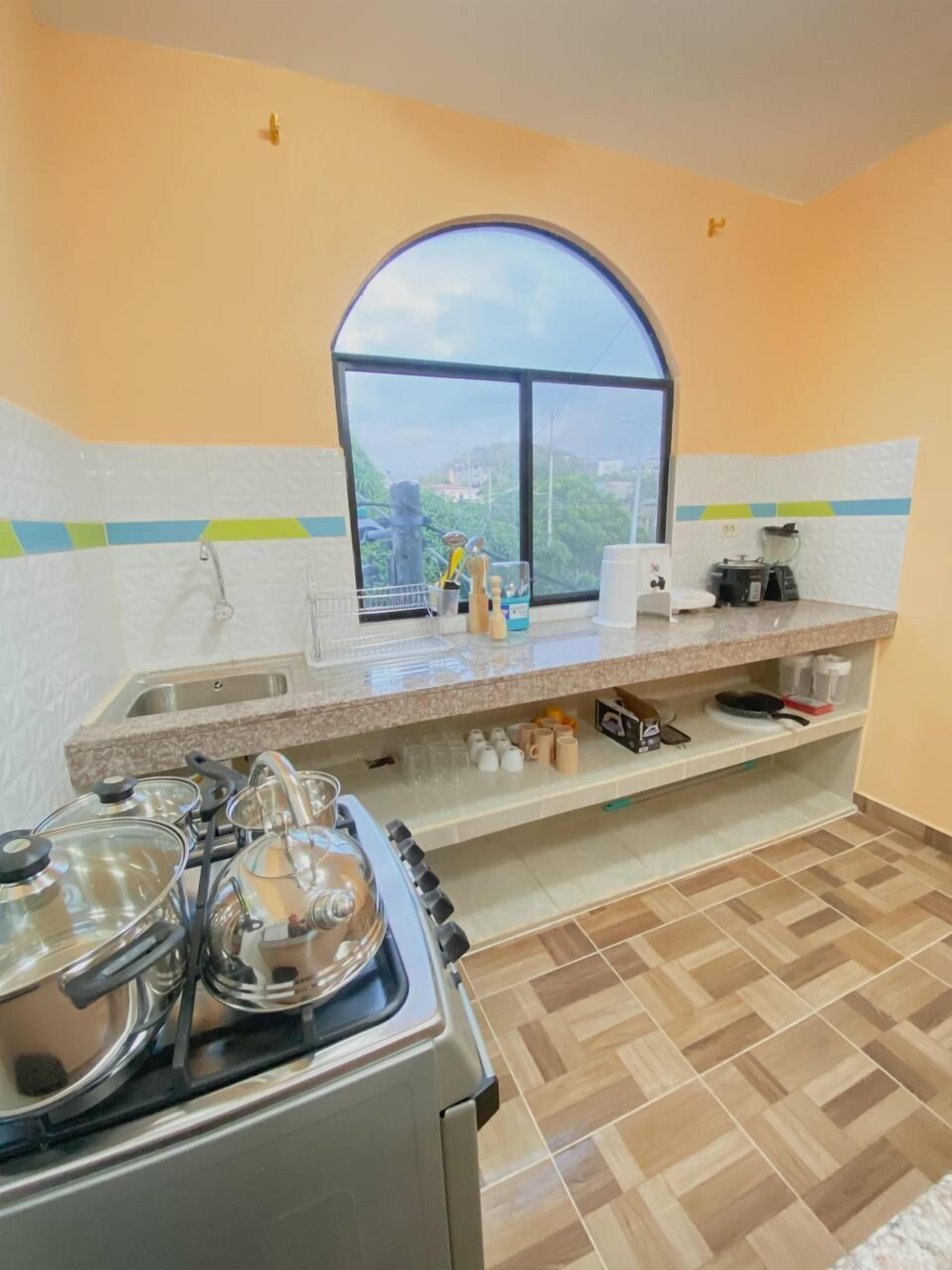 A kitchen with a gas stove, a sink, a window with a view, and a countertop with various items.