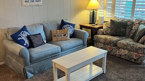 Un salon avec un canapé gris, une table basse blanche et un mur orné d’une décoration sur le thème de la plage.