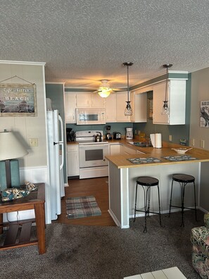 A compact kitchen with white cabinets, a microwave, a stove, and a small island with stools. - Cozy Condo in Ocean City steps from the beach (Ocean City)