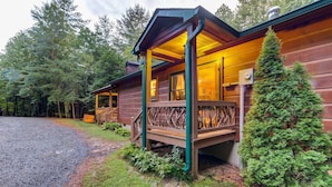 Une cabane dotée d’une véranda, d’une cheminée et entourée d’une forêt.