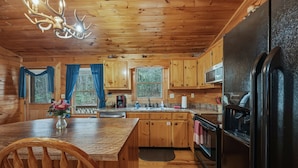 Une cuisine rustique aménagée dans une cabane en bois, avec une table à manger, des chaises, un réfrigérateur et un four à micro-ondes.