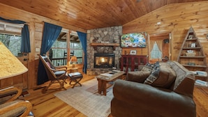 L’intérieur d’un chalet accueillant, avec une cheminée en pierre, des meubles en bois et un téléviseur.