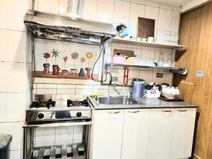A kitchen with a gas stove, a sink, and white cabinets. There are shelves above the sink with various items. - [2026/4 NEW RENOVATION] Bright Large Window Ensuite Quiet Cozy Room-1 Min to MRT (Taipei City)