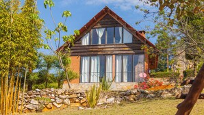 Una casa de madera con ventanas amplias, un muro de piedra y un jardín con rocas y plantas.