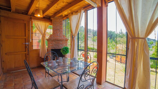 Un comedor con una mesa de vidrio y sillas de metal, una chimenea de ladrillo y vistas al exterior.