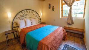 Un dormitorio con cama, mesitas de noche, una ventana con cortinas y un banco.