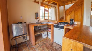 Una cocina compacta con refrigerador, estufa y lavamanos, armarios de madera y un ventanal con cortinas.