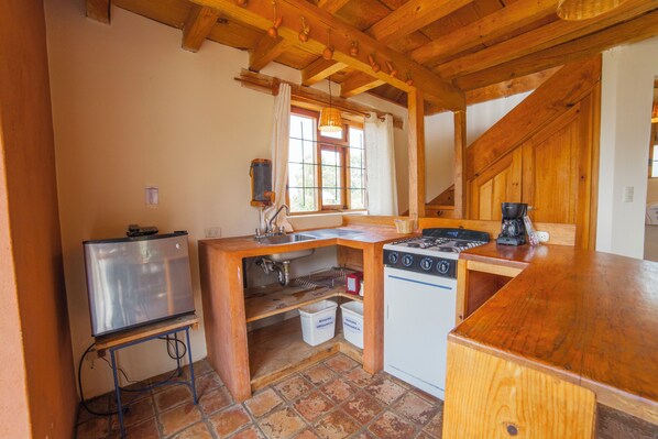A compact kitchen with a refrigerator, stove, and sink, wooden cabinets, and a window with curtains.