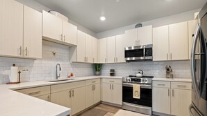 A modern kitchen with light-colored cabinets, stainless steel appliances, and a white countertop.