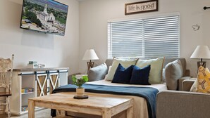 A bedroom with a bed, bedside tables, a desk, a chair, a window with blinds, and a painting on the wall.