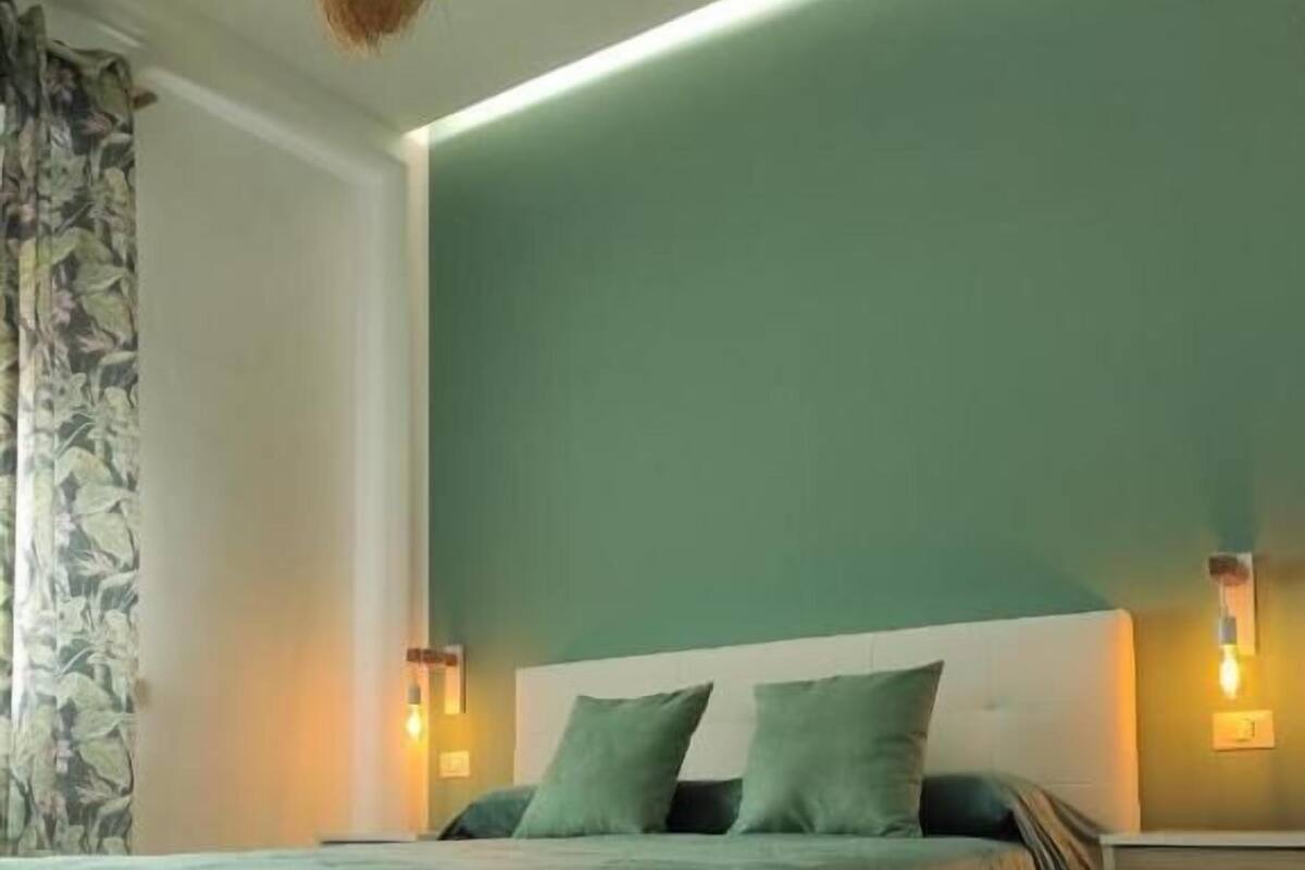 Ein modernes Schlafzimmer mit einer grünen Bettdecke, Holzboden und einem Nachttisch mit Lampe.