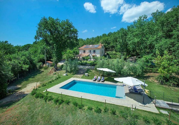 Una casa con piscina, circondata da un lussureggiante verde e un cielo azzurro.