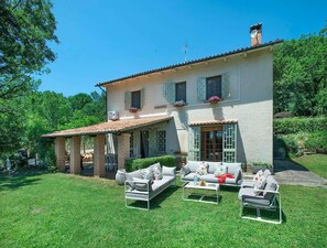 Una casa a due piani con patio, mobili da giardino e un giardino.