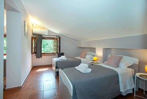 Una camera d'albergo con due letti, una finestra con tende, un comodino con una lampada e un piccolo riscaldatore.