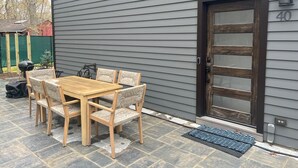 Eine Terrasse mit einem Holztisch und Stühlen, eine Tür mit einer Hausnummer und ein Briefkasten.
