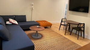 Ein modernes Wohnzimmer mit einer Couch, einem Hocker, einem Couchtisch und einem an der Wand befestigten Fernseher.