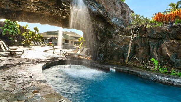Un espace piscine agrémenté d’une cascade, de chaises longues et d’une terrasse dallée de pierres.