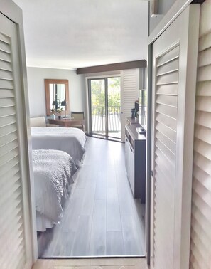 Een hotelkamer met twee bedden, een bureau, een dressoir en een schuifpui naar een balkon.