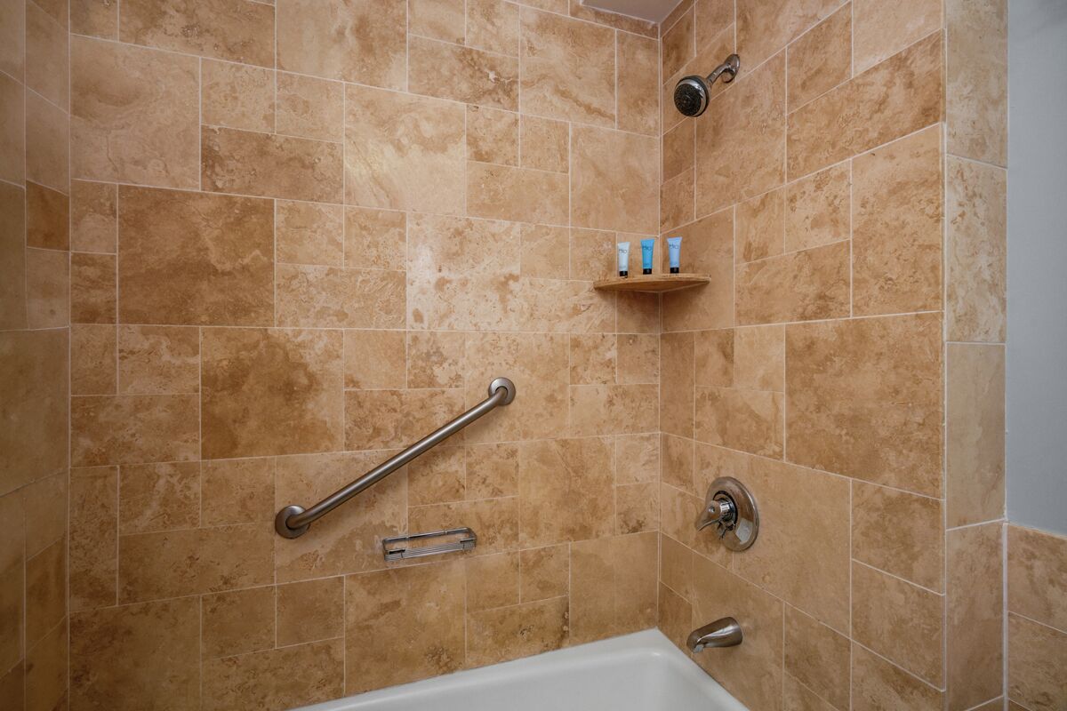 A bathroom with beige tiles, a shower, a bathtub, and a shelf with toiletries.
