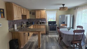 Una cocina con armarios de madera, encimera de granito, microondas, refrigerador y un comedor con mesa y sillas.