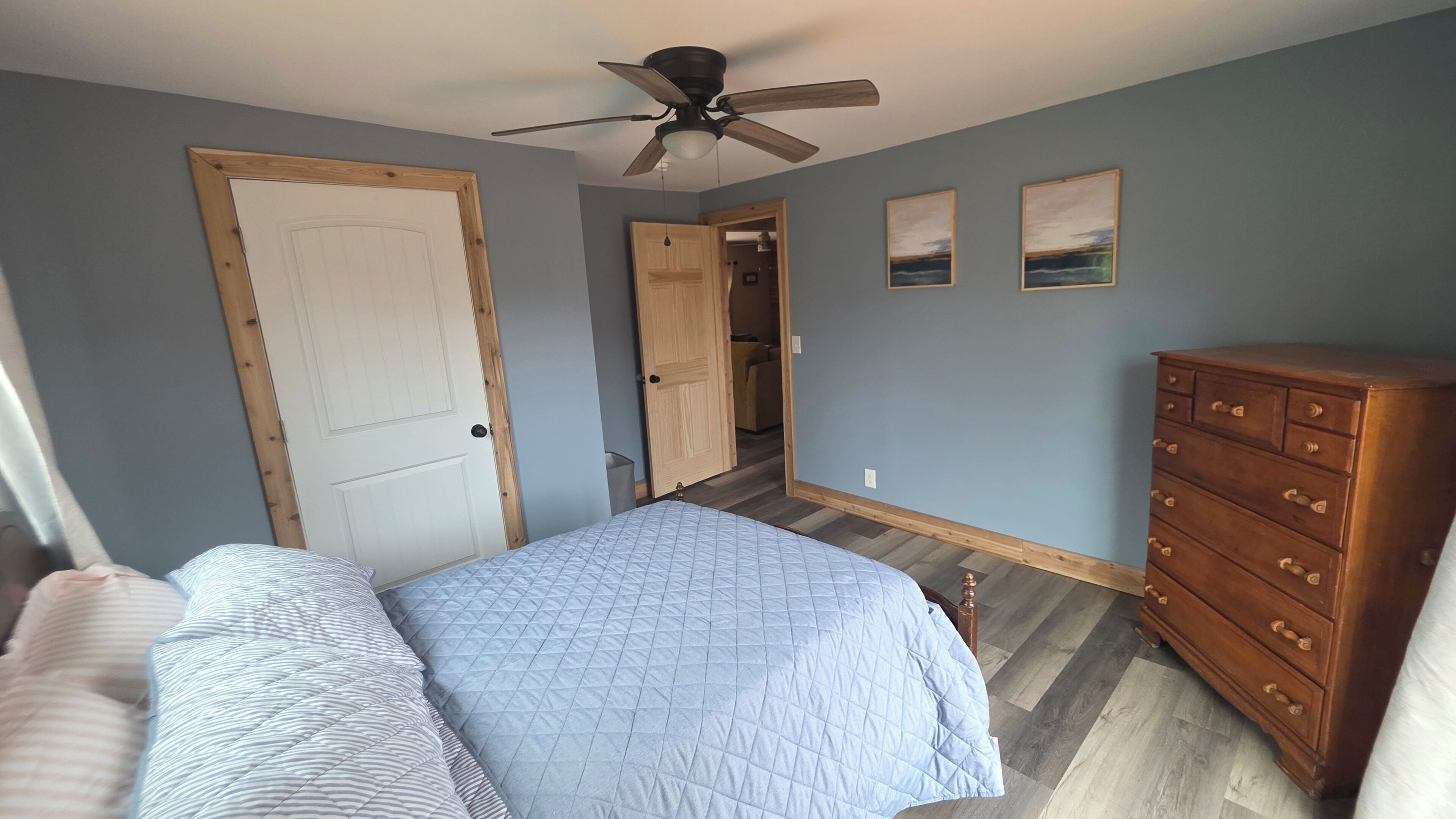A bedroom with a bed, dresser, ceiling fan, and two doors leading to other rooms.