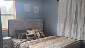 Un dormitorio con cama, ventilador de techo, ventana y mesita de noche.