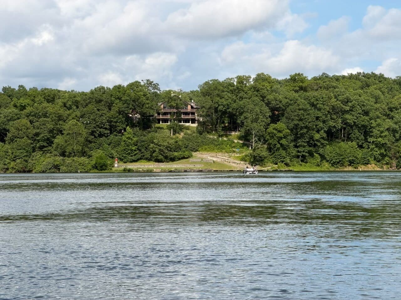 A lake with a building on a hill, surrounded by trees.