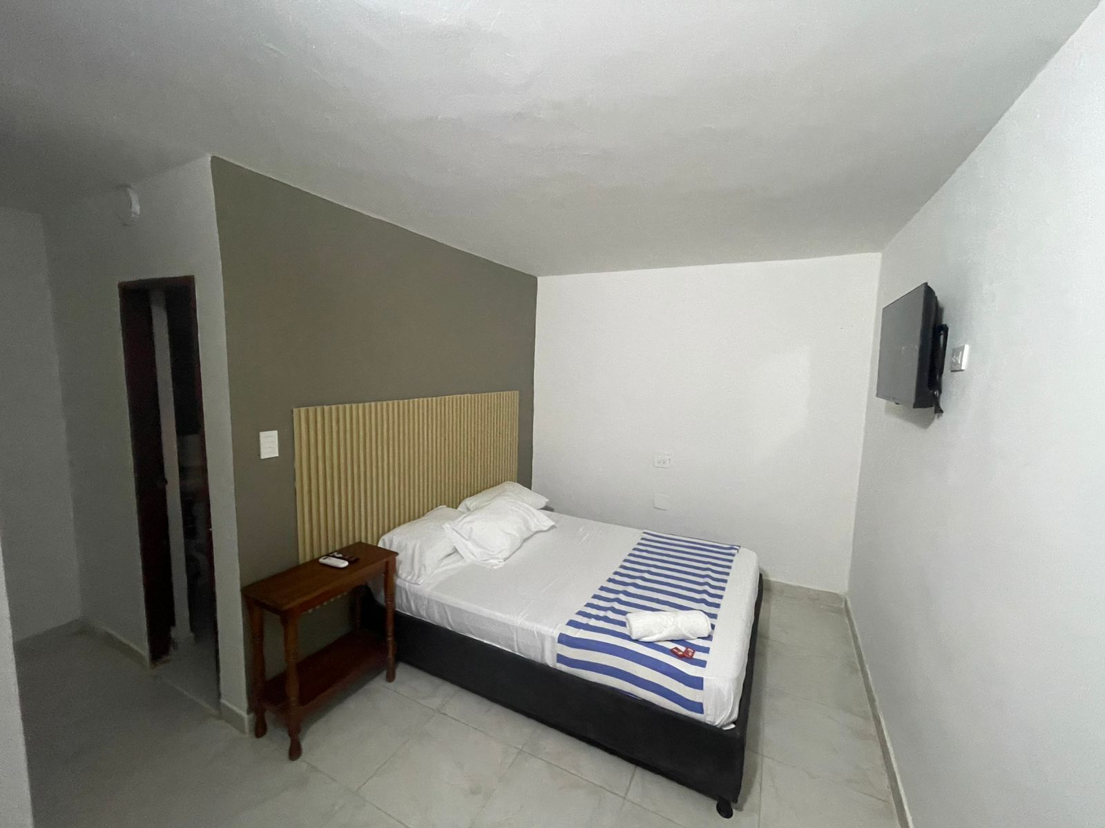 A small, clean room with a single bed, a nightstand, and a TV mounted on the wall.