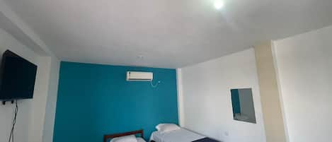 A room with three beds, a flat-screen TV, and a ceiling light.