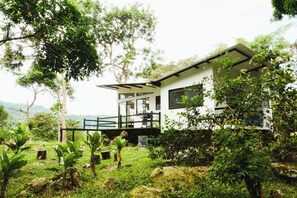 Una casa moderna con balcón, rodeada de exuberante vegetación y árboles.
