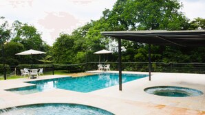 Piscina com área circular embutida, rodeada por um espaço coberto com guarda-sóis.