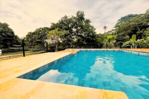 A rectangular swimming pool with a tiled edge, surrounded by a wooden deck and a metal fence.