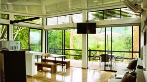 Um quarto espaçoso com uma grande porta de vidro deslizante que dá para uma varanda, uma mesa de madeira com bancos e um sofá.