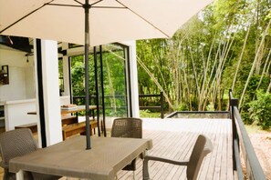 An outdoor deck with a table and chairs, a large umbrella, and a view of a bamboo forest.