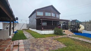 Een houten huis met twee verdiepingen, een overdekte veranda en een kleine speelruimte met een glijbaan.