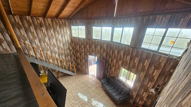 Een ruime loft met een hoge plafond, houten wanden, een ingebouwde trap en grote ramen met uitzicht.