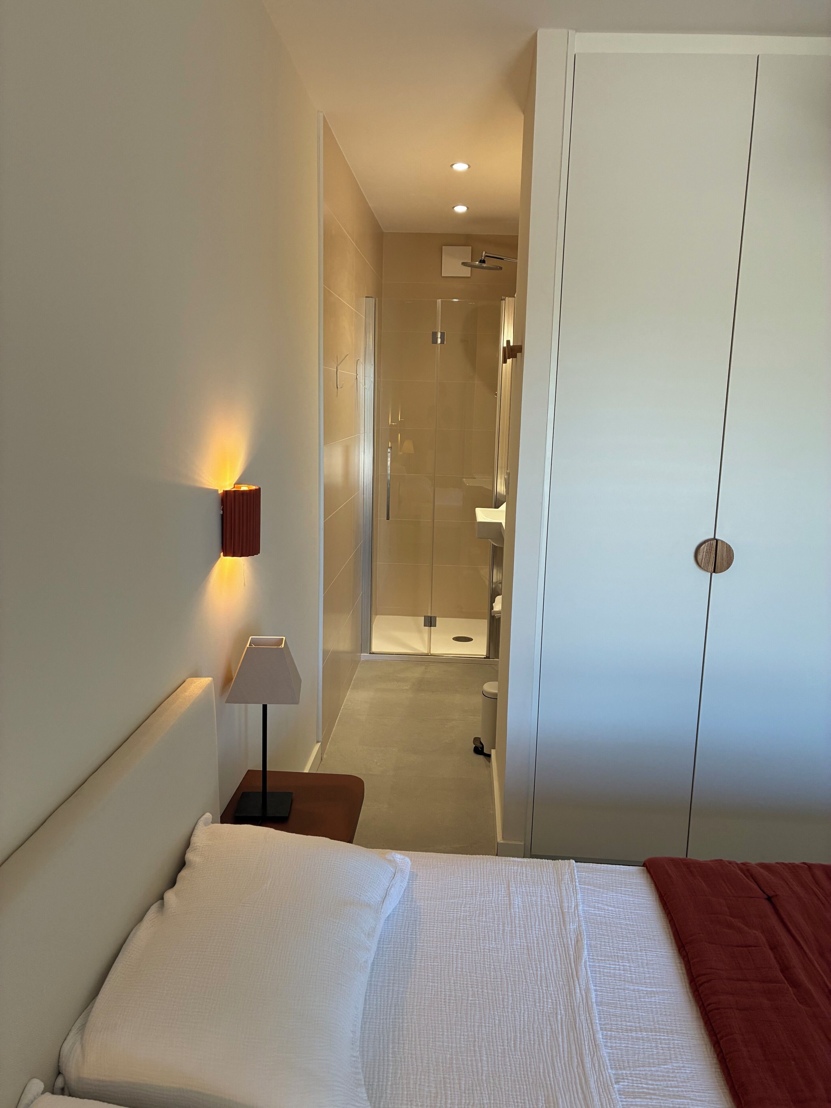 A hotel room with a bed, a bedside lamp, a wardrobe, and a shower area.