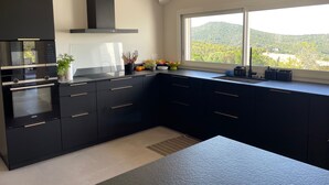 Eine moderne Küche mit schwarzen Schränken, einem eingebauten Backofen und einem Fenster mit Blick auf eine gebirgige Landschaft.