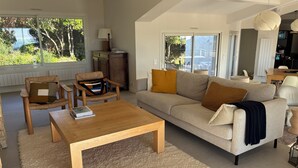 Ein modernes Wohnzimmer mit einer Couch, Sesseln, einem Couchtisch und einem Essbereich mit Tisch und Stühlen.